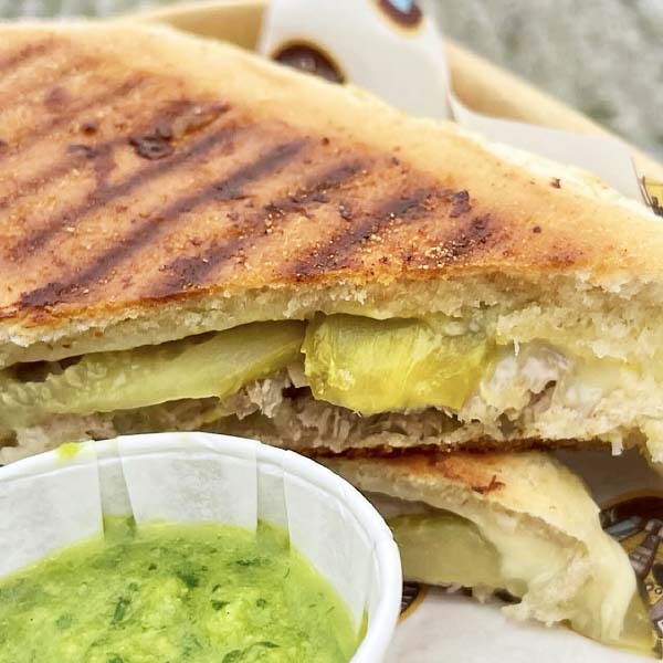 Toasted Cubano sandwich filled with roast pork, ham, Swiss cheese, pickles, and mustard, served street food style from The Clippy.