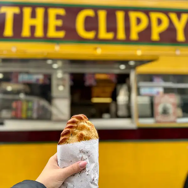 A customer holding a Home Made Rump Steak Pasty in front of The Clippy, Plymouth's street food bus by Fletcher's Restaurant.